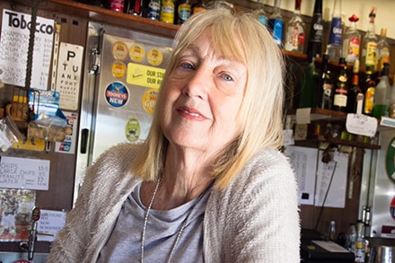 A woman with blond hair leaning on the bar of a pub.