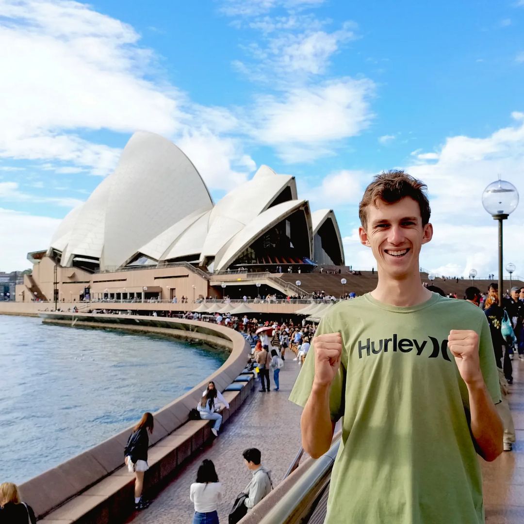 A man fist pumps in front of the Sydney Opera House.
