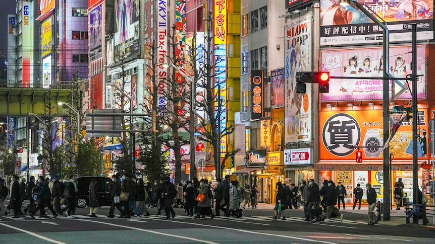 People cross a busy intersection at night in Tokyo.