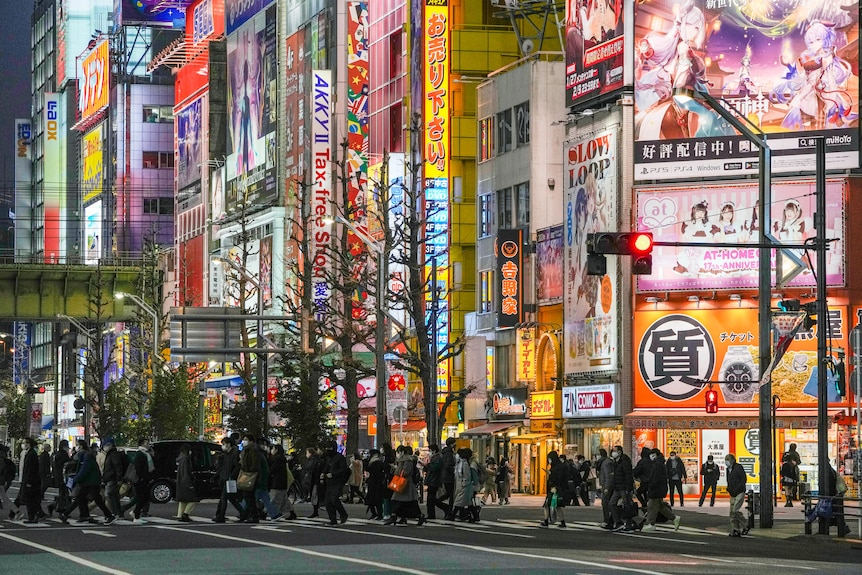 People cross a busy intersection at night in Tokyo.