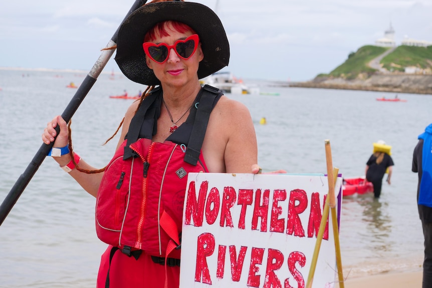 A woman holding a paddle next to a sign that reads 'Northern Rivers'.