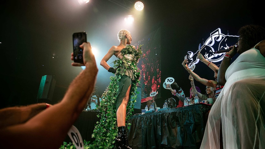 A ballroom competitor in green, floral costume and short blonde hair poses for the judges on the runway at Sissy Ball 2019.