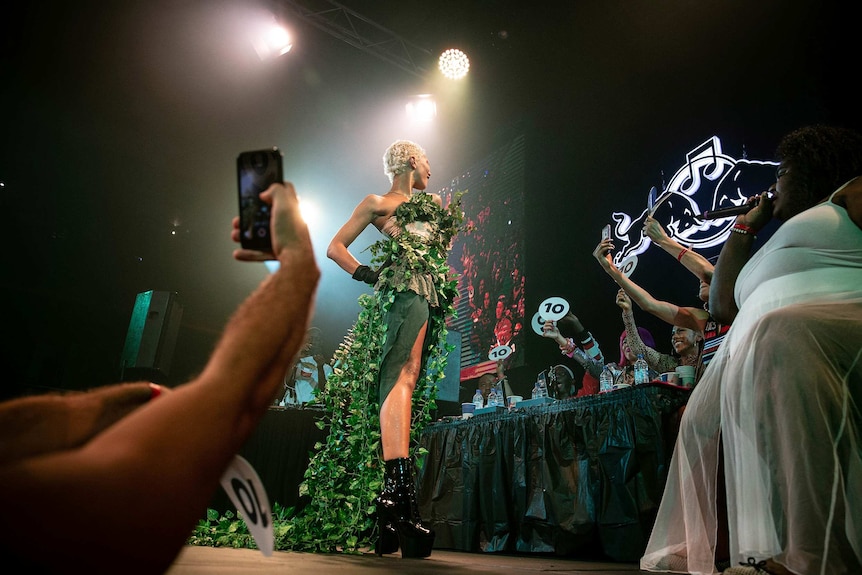 A ballroom competitor in green, floral costume and short blonde hair poses for the judges on the runway at Sissy Ball 2019.