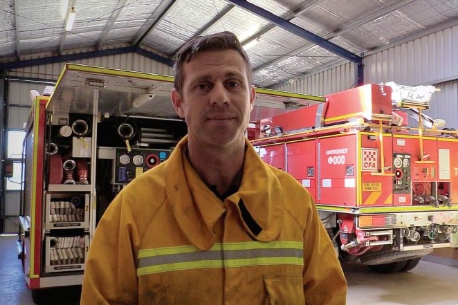 A man dressed in fire fighting clothes and a fire truck behind him