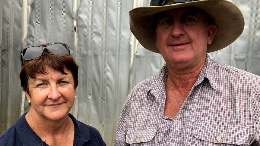 Two farmers, a woman and a man, stand in front of their fire-damaged property