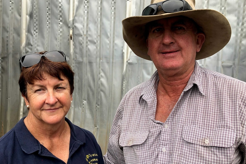 Two farmers, a woman and a man, stand in front of their fire-damaged property