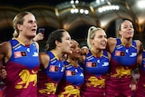 Brisbane Lions players stand arm-in-arm next to each other singing