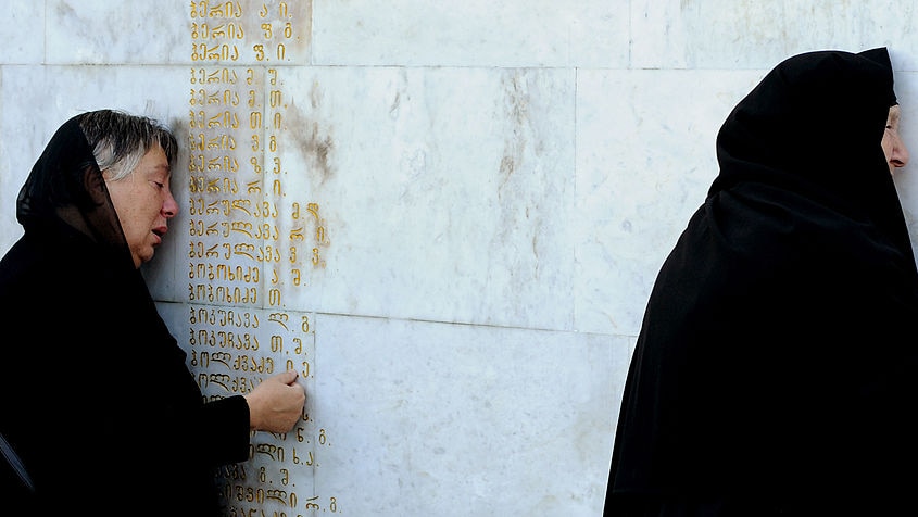 Women dressed in black grieve at a war memorial listing the names of killed soldiers.