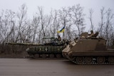A Ukrainian serviceman in a tank prepares to shoot while his comrade passes by in an armoured vehicle.