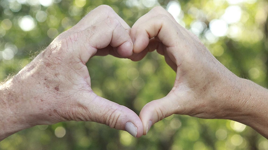 An older couple make heart made from their hands.