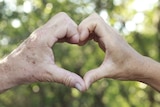 An older couple make heart made from their hands.