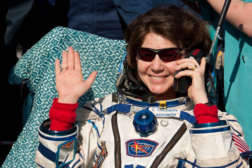 Woman in astronaut suit talks on phone while smiling and waving