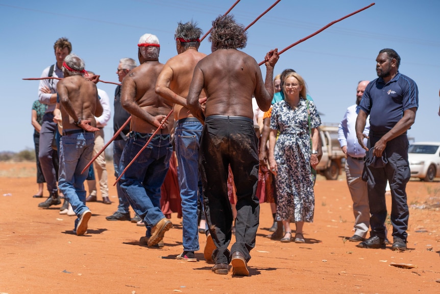 A woman looks on as a group of men hold speers. 