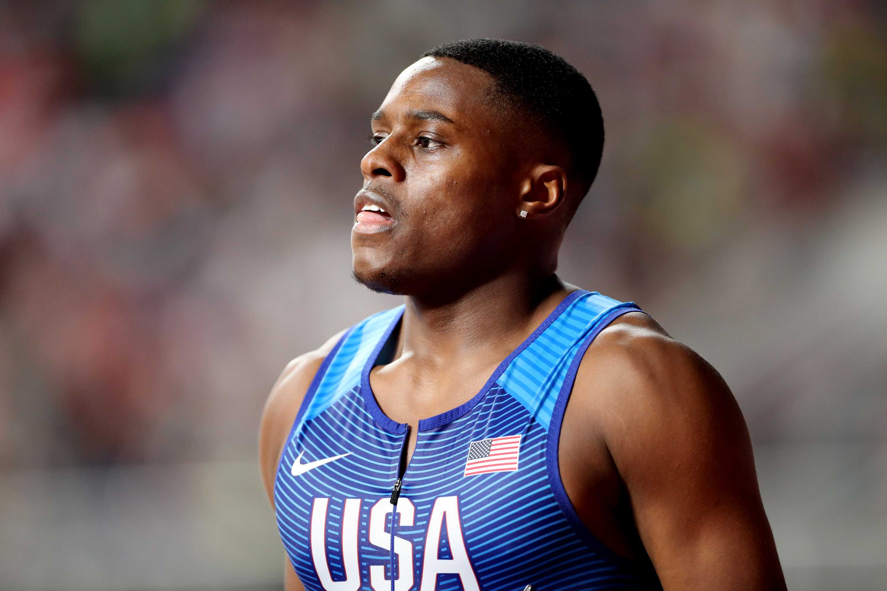 Christian Coleman olha para o lado vestindo uma camiseta azul justa com 'EUA' escrito na frente