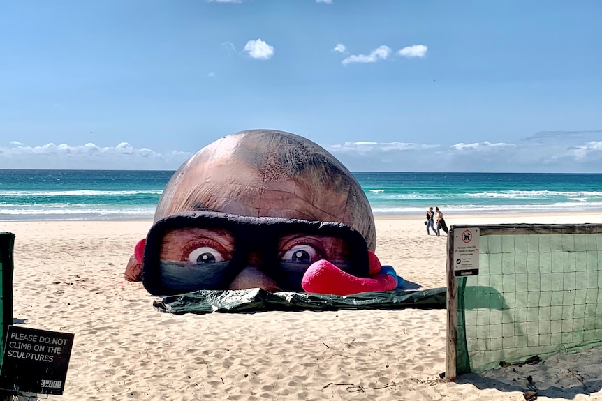 A large sculpture of a head wearing goggles with a snorkel on the sand