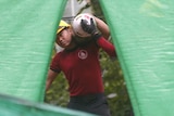 A man in a red shirt carrying an oxygen tank.