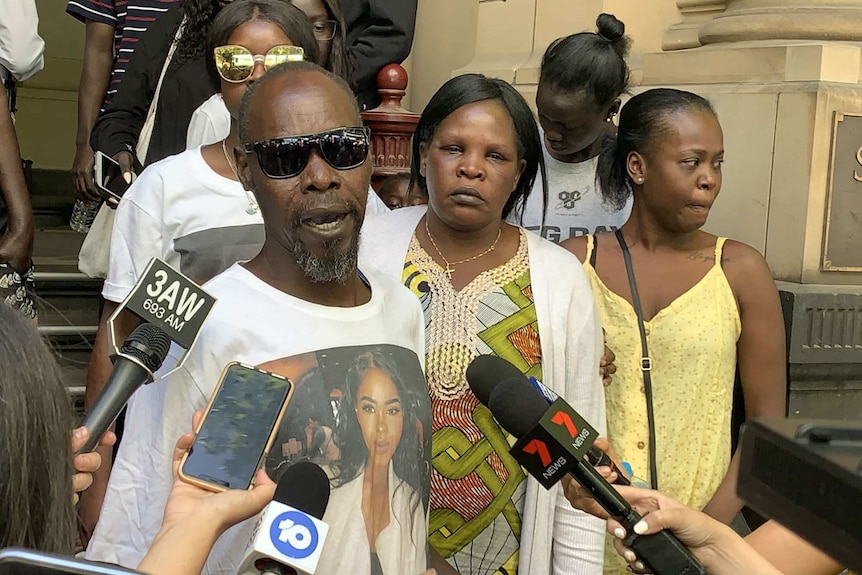 Daniel Kunyrieth Chol stands outside court wearing a shirt with his daughter Laa Chol on it.