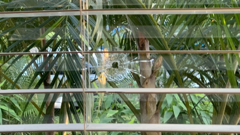 A window that has been shot through, seen through blinds.