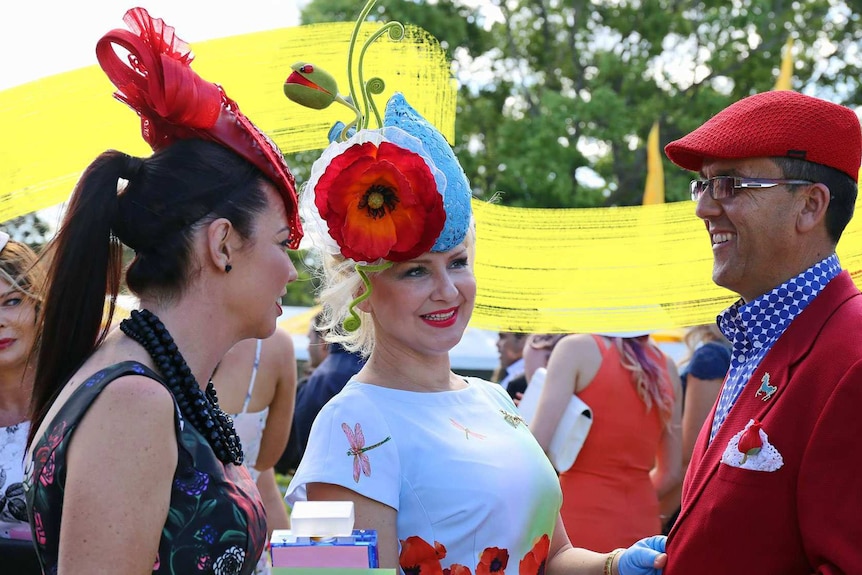 Women in hats smiling at man in red suit for a story about the ethics of horseracing and Melbourne Cup.