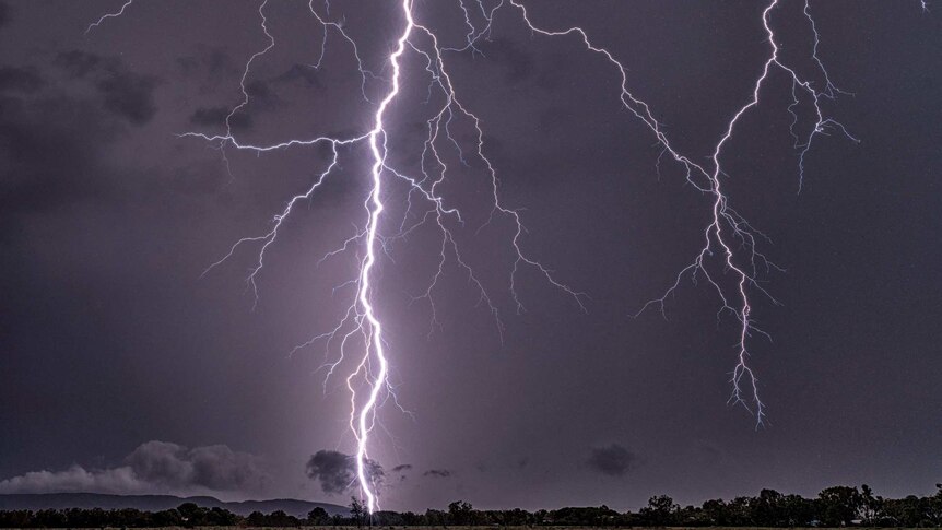 Lightning bolts captured striking the earth above an outback landscape.