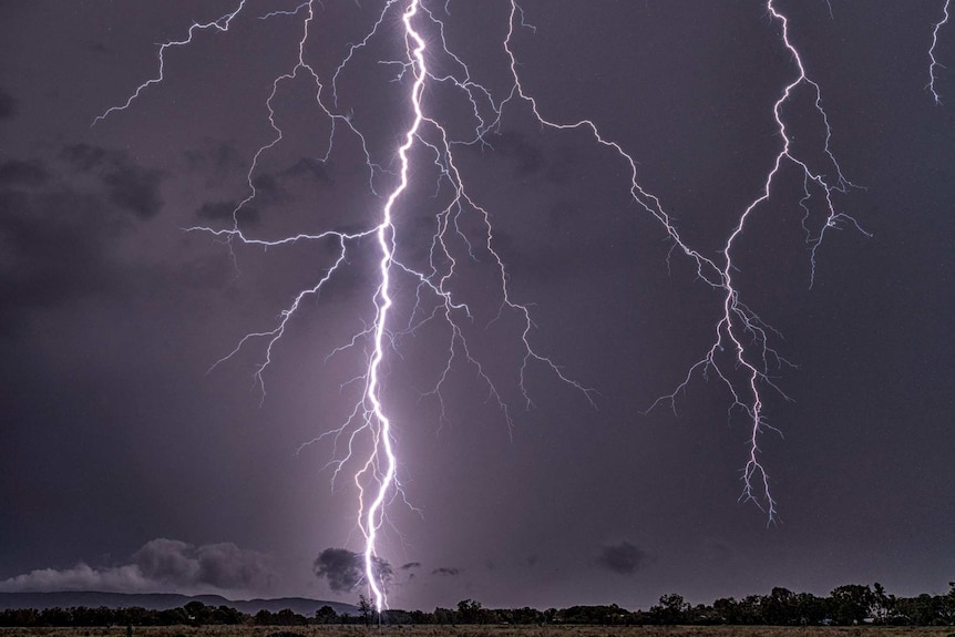 Lightning bolts captured striking the earth above an outback landscape.