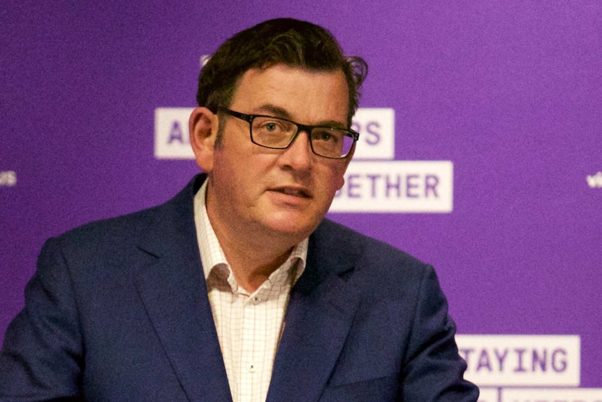 Daniel Andrews speaks at a podium with one hand raised.