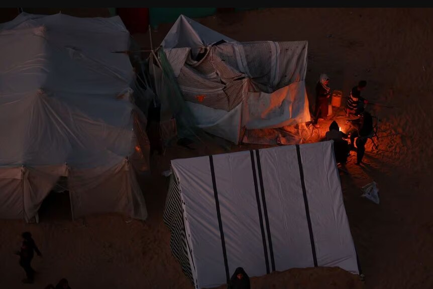 People huddling around large tents and a fire