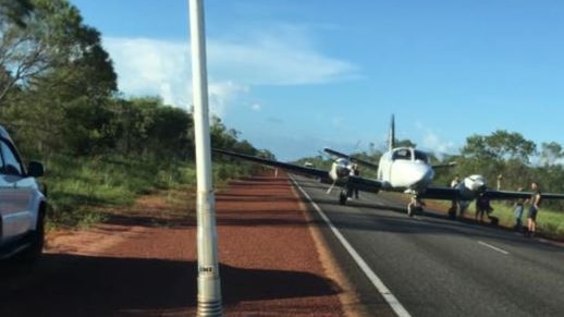 A small plane without damage sits in the middle of a highway in remote WA with people around it.