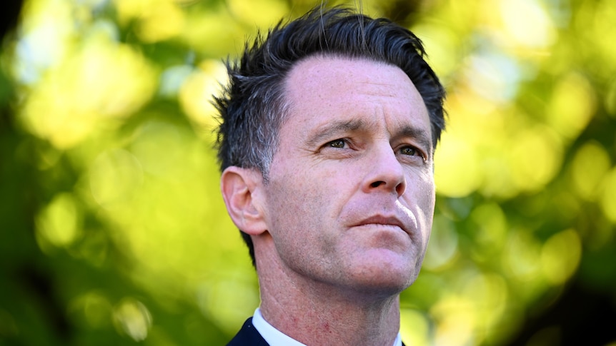 A portrait shot of a clean-shaven man with black hair, outdoors.