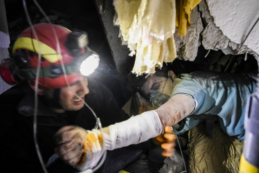 A firefighter holds a man's hands which is trapped in the rubble of a building struck by an earthquake.