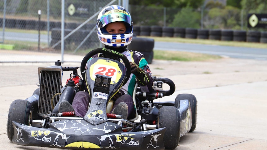 A boy sits in a kart with his helmet on.