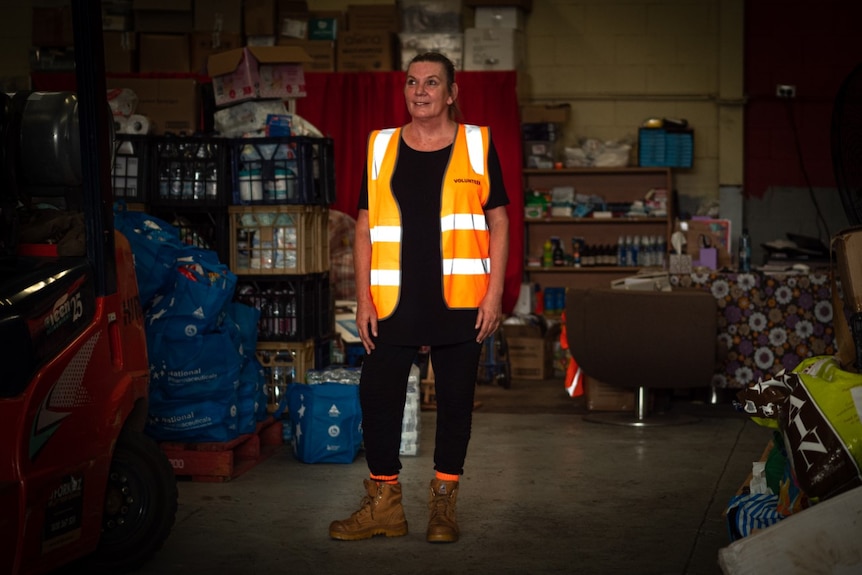 A smiling woman wearing a bright orange vest and boots.