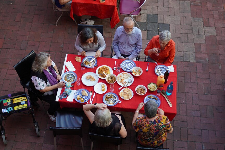 People sitting around a table with food and a red tablecloth from above