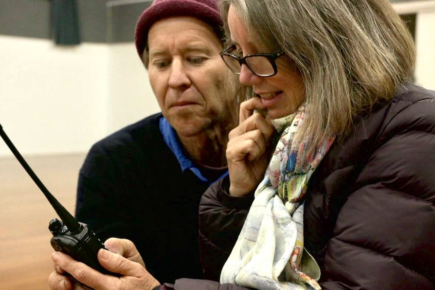 Two people sit side by side looking at a hand held radio.