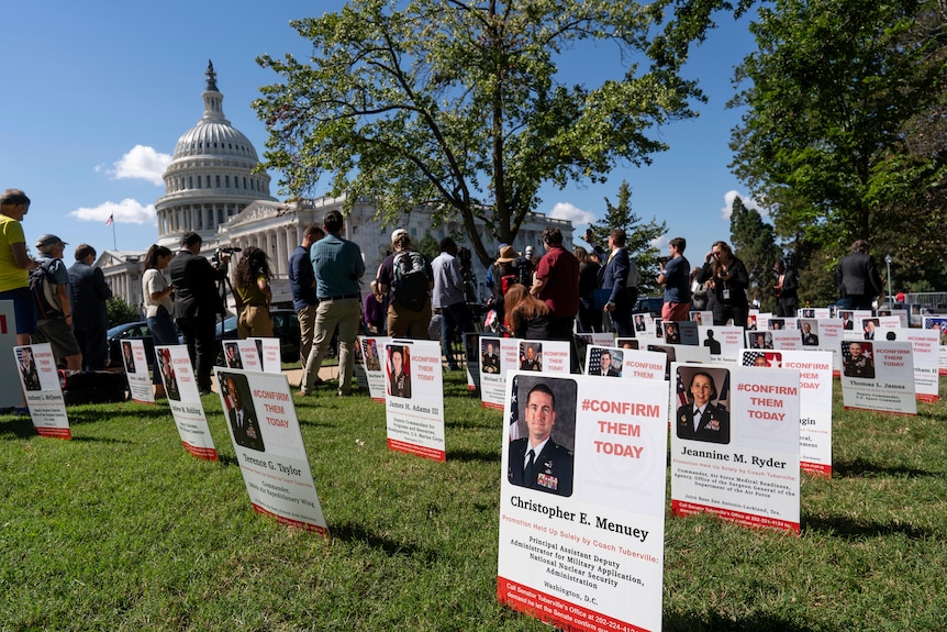 Signs displaying the faces of military members with the words 'confirm them today' are placed in the lawn near the Capitol.