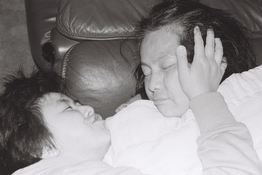 A black-and-white photograph shows a woman and child embracing on a couch. The child has a hand on the woman's face.