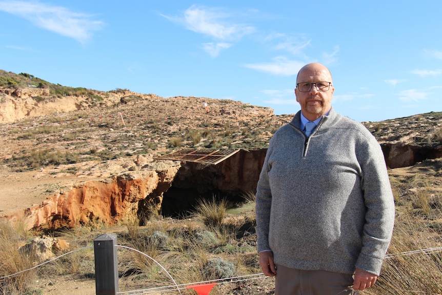 A man in a cardigan standing in front of a cliff hole