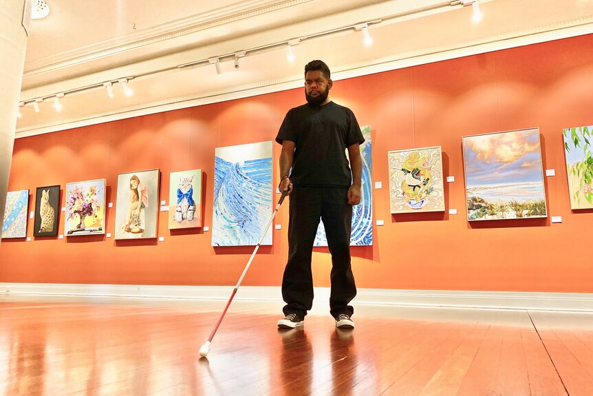Indigenous man in black with cane in art gallery space