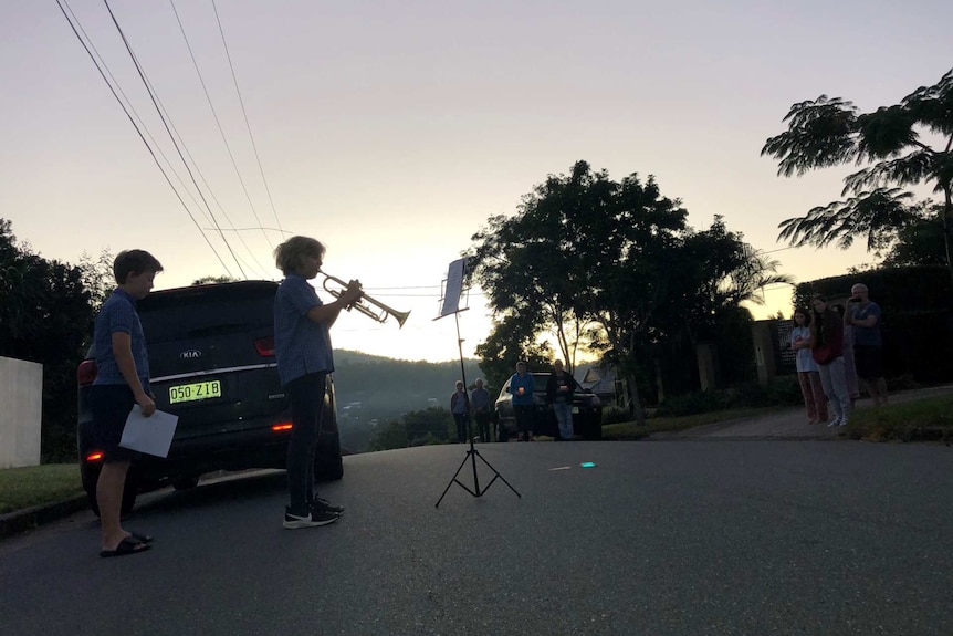 a boy holds a trumpet with another boy standing behind him in the street as neighbours gather.