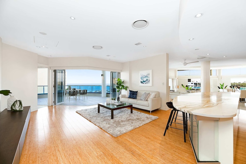 A photo of a Sunshine Coast seaside penthouse, showing the lounge room, kitchen and balcony.
