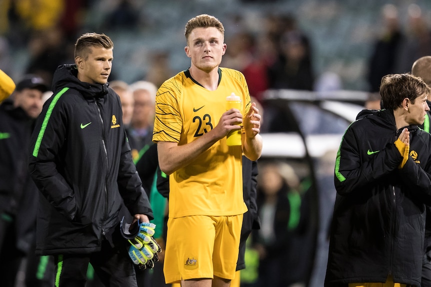 An Australian footballer in a Socceroos shirt claps the crowd after a game.