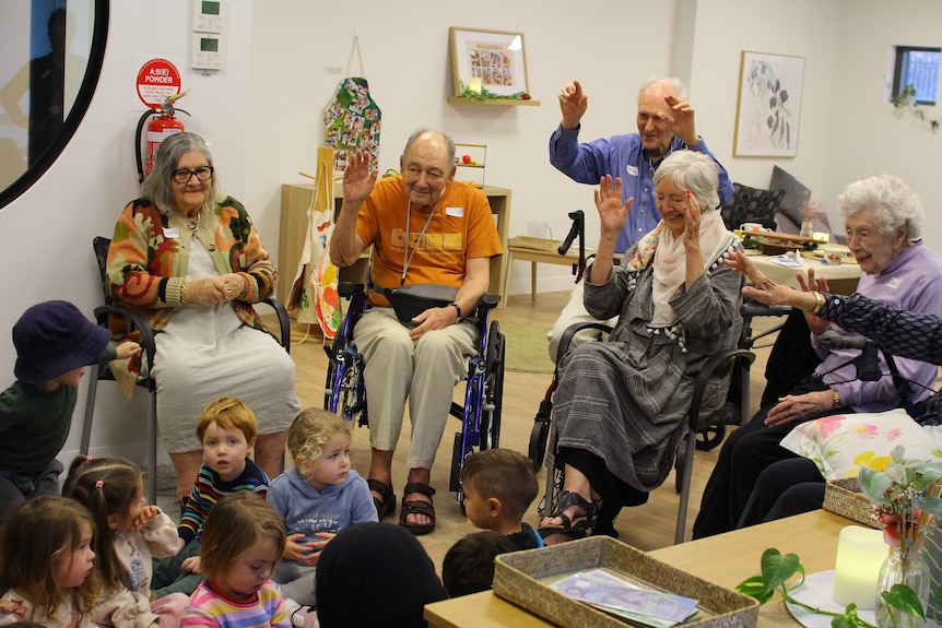A group of aged-care residents with toddlers, happy with their hands in the air