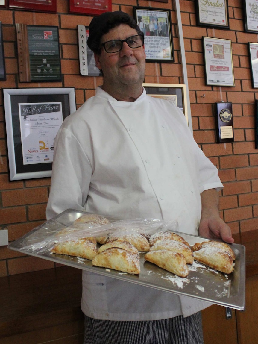 A chef hold holding a large metal tray covered with sugar-dusted apple turnovers.