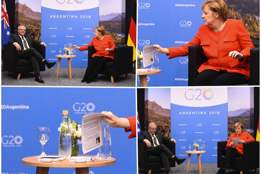 Angela Merkel sitting at a table with Scott Morrison. In Ms Merkel's hand is a piece of a paper with a photo of Mr Morrison.