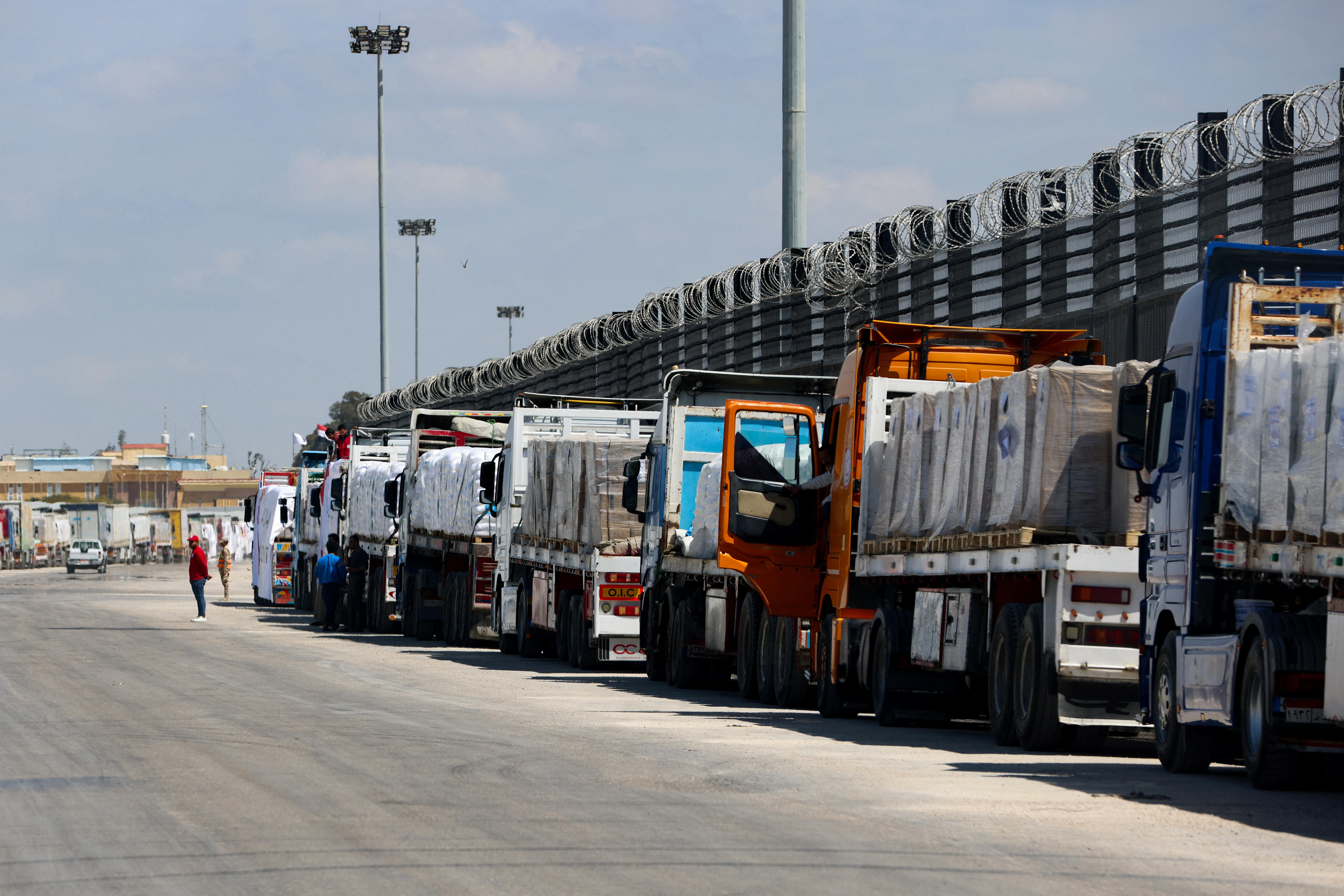 A line of trucks on the side of a road next to a fence.