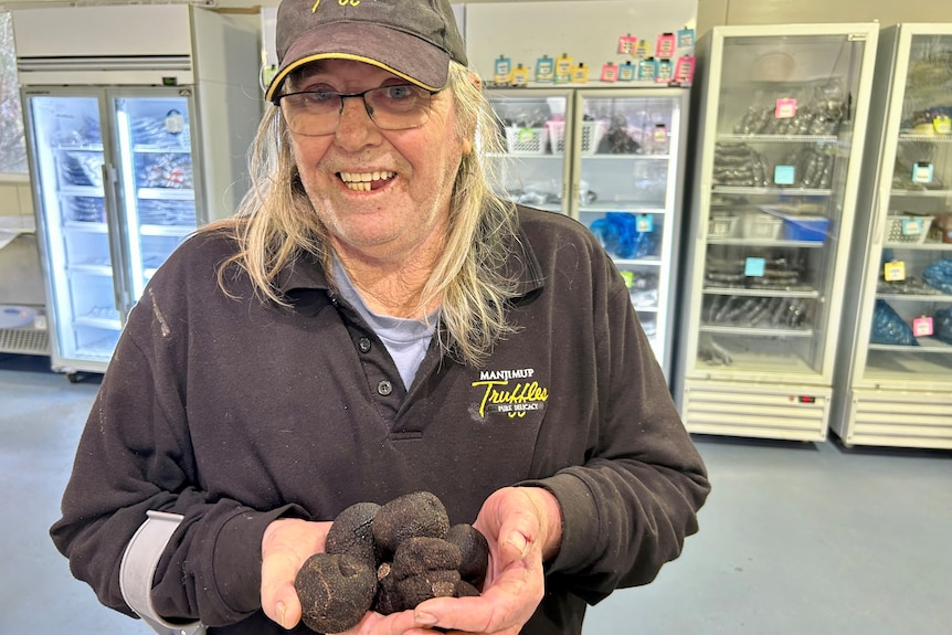 A man in a black shirt poses for a photo holding a handful of small black lumps 