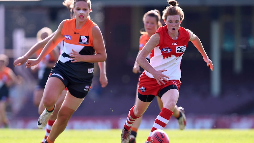 GWS Giants and Sydney Swans women's AFL players chase a ball.