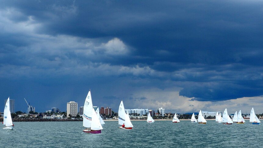 Front on, water level view of the fleet racing towards a mark with a dark storm cloud overhead.