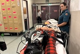 A girl lays on a hospital trolley with a paramedic watching over her
