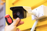 A small security camera being installed on a yellow wall